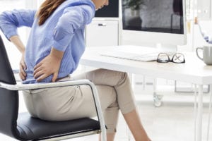 Business woman with back pain sitting in chair in need of decompression therapy