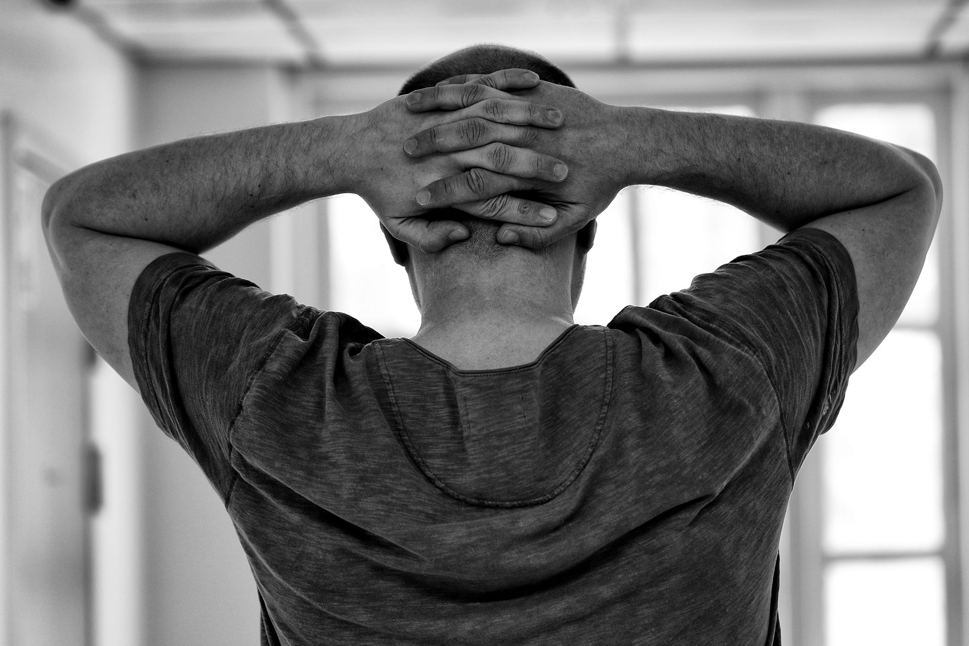 Black and white picture of guy from behind with hands interlaced on the back of his from a tension headache and neck pain