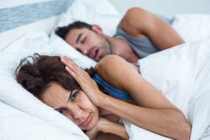Woman lying in bed with ears covered from husband snoring who needs sleep apnea treatment