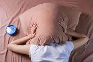 woman with a migraine headache covering her head with a pillow