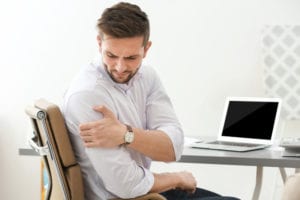 Man sitting at desk in pain due to a pinched nerves in his shoulder