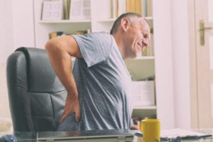Man grabbing his lower back while sitting at a desk because he needs treatment for degenerative disc disease
